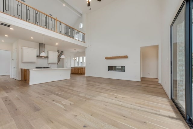 unfurnished living room with light wood-type flooring, a high ceiling, visible vents, and a glass covered fireplace