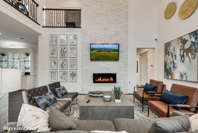 living area featuring a stone fireplace, wood finished floors, and a high ceiling