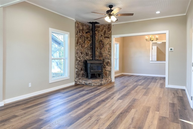 unfurnished living room featuring ceiling fan with notable chandelier, wood-type flooring, a wood stove, and ornamental molding