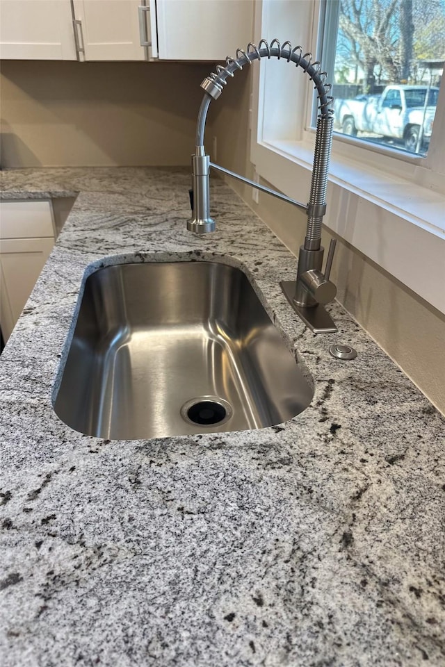 room details with white cabinets, light stone counters, and sink