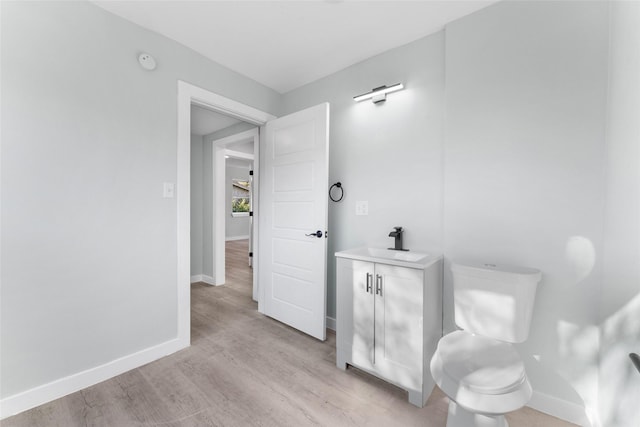 half bath with vanity, toilet, wood finished floors, and baseboards