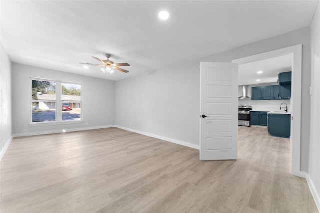 empty room with a ceiling fan, light wood-type flooring, baseboards, and a sink