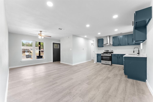 kitchen featuring visible vents, light wood finished floors, a sink, stainless steel gas range oven, and wall chimney exhaust hood