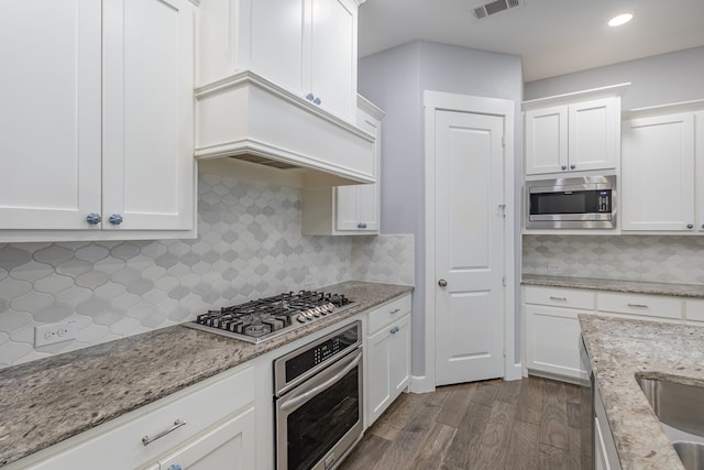 kitchen with dark wood-type flooring, light stone counters, backsplash, white cabinetry, and appliances with stainless steel finishes