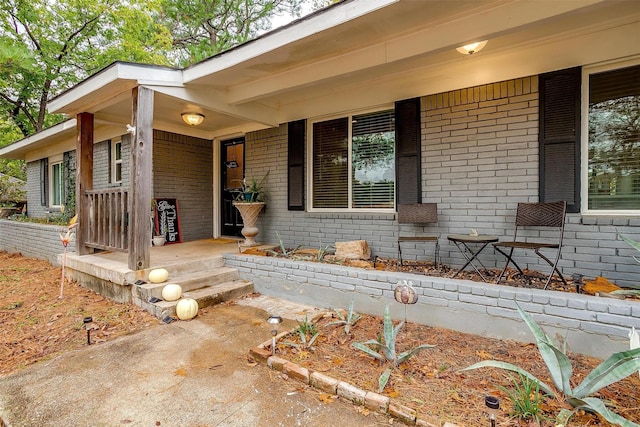 view of exterior entry featuring covered porch and brick siding