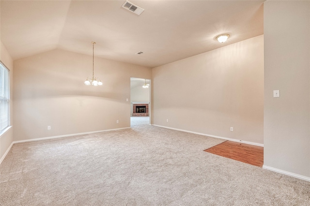 spare room featuring carpet floors, a brick fireplace, lofted ceiling, and a chandelier