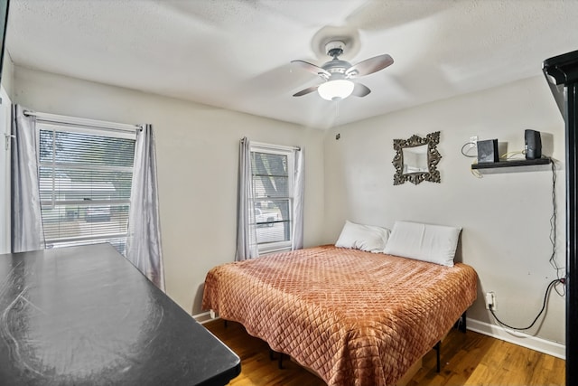 bedroom with a textured ceiling, multiple windows, wood-type flooring, and ceiling fan