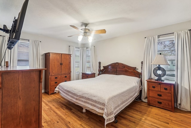 bedroom featuring multiple windows, a textured ceiling, light wood-type flooring, and ceiling fan