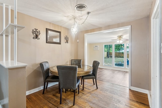 dining space featuring a textured ceiling, wood-type flooring, and ceiling fan with notable chandelier