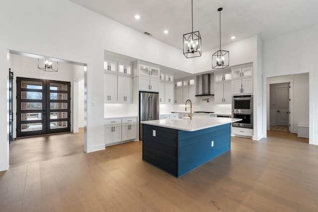 kitchen featuring light hardwood / wood-style flooring, wall chimney range hood, a high ceiling, and an island with sink