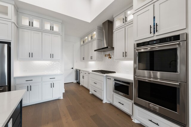 kitchen featuring decorative backsplash, dark hardwood / wood-style floors, wall chimney exhaust hood, white cabinetry, and appliances with stainless steel finishes