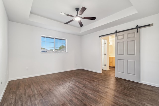 unfurnished bedroom featuring a raised ceiling, a barn door, dark hardwood / wood-style floors, and ceiling fan