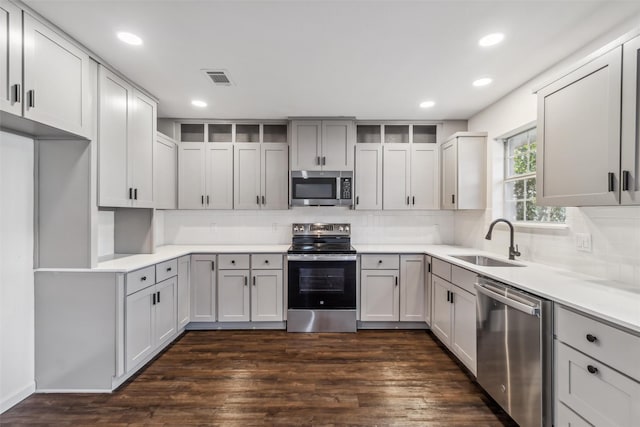 kitchen with sink, appliances with stainless steel finishes, dark hardwood / wood-style floors, gray cabinets, and decorative backsplash