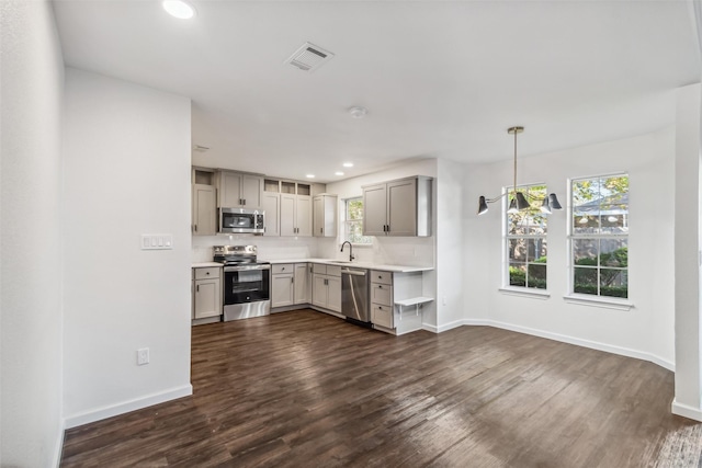 kitchen with sink, appliances with stainless steel finishes, dark hardwood / wood-style floors, gray cabinets, and pendant lighting