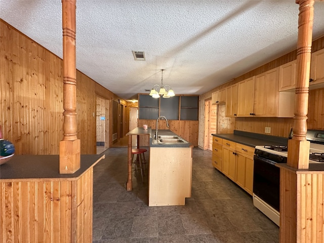 kitchen with an island with sink, a kitchen bar, sink, wooden walls, and white gas range oven