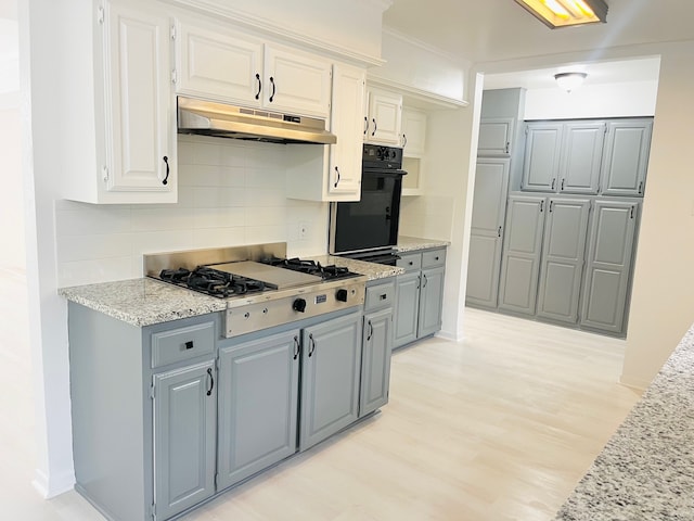 kitchen with decorative backsplash, stainless steel gas cooktop, oven, light stone counters, and light hardwood / wood-style floors