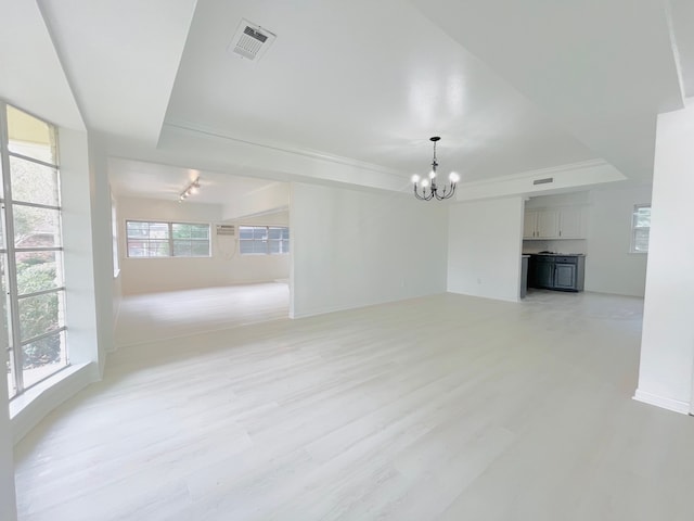 unfurnished living room featuring light hardwood / wood-style floors, a notable chandelier, and a raised ceiling