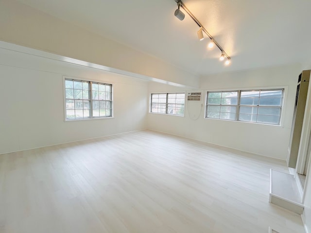 empty room with an AC wall unit, light hardwood / wood-style floors, and rail lighting