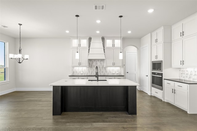 kitchen with sink, custom exhaust hood, white cabinets, oven, and backsplash