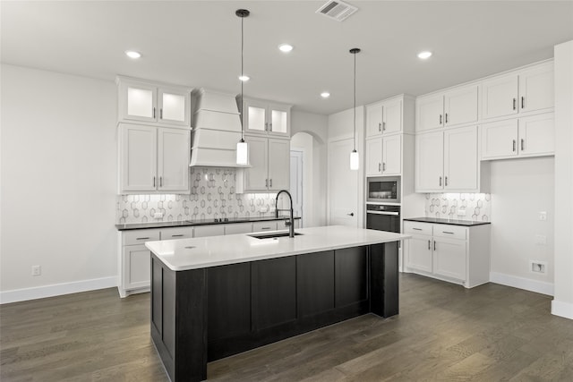 kitchen featuring pendant lighting, sink, white cabinets, a center island with sink, and built in microwave