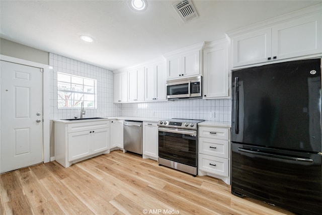 kitchen featuring white cabinets, tasteful backsplash, appliances with stainless steel finishes, light hardwood / wood-style flooring, and sink