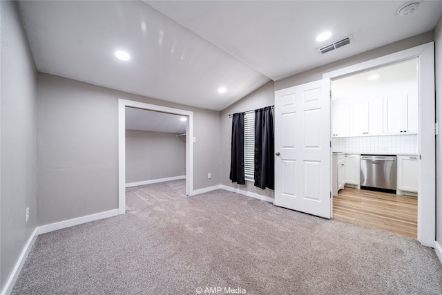 unfurnished bedroom featuring a spacious closet, ensuite bath, lofted ceiling, and light colored carpet