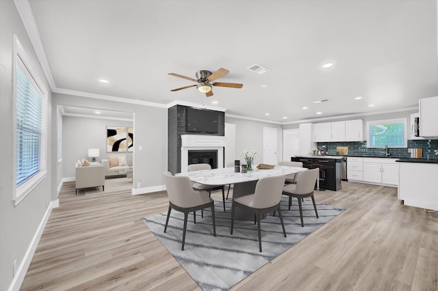 dining space featuring sink, a large fireplace, ornamental molding, ceiling fan, and light hardwood / wood-style flooring