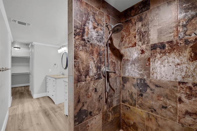 bathroom with vanity, tiled shower, ornamental molding, and wood-type flooring