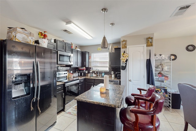 kitchen featuring light tile patterned floors, appliances with stainless steel finishes, decorative light fixtures, and a kitchen island