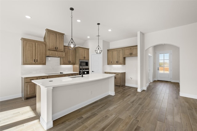 kitchen with hardwood / wood-style floors, stainless steel microwave, black electric stovetop, sink, and an island with sink