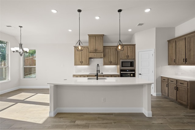 kitchen with stainless steel microwave, black oven, sink, backsplash, and a large island with sink