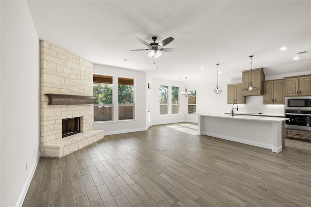 unfurnished living room featuring sink, dark hardwood / wood-style flooring, ceiling fan with notable chandelier, and a stone fireplace