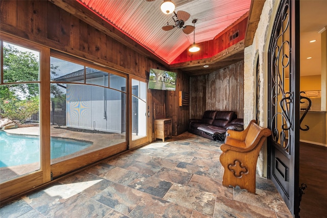 living area with ceiling fan, wooden ceiling, vaulted ceiling, and wooden walls