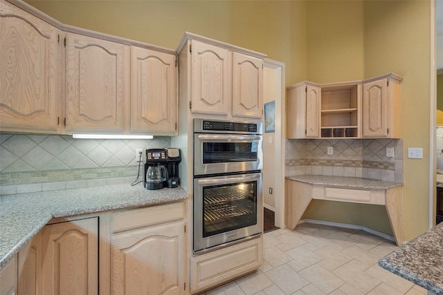 kitchen featuring light stone countertops, tasteful backsplash, light brown cabinetry, and double oven