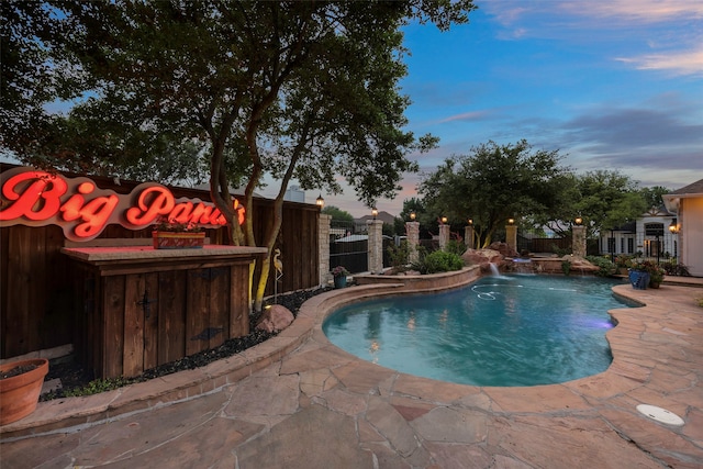 pool at dusk featuring pool water feature and a patio