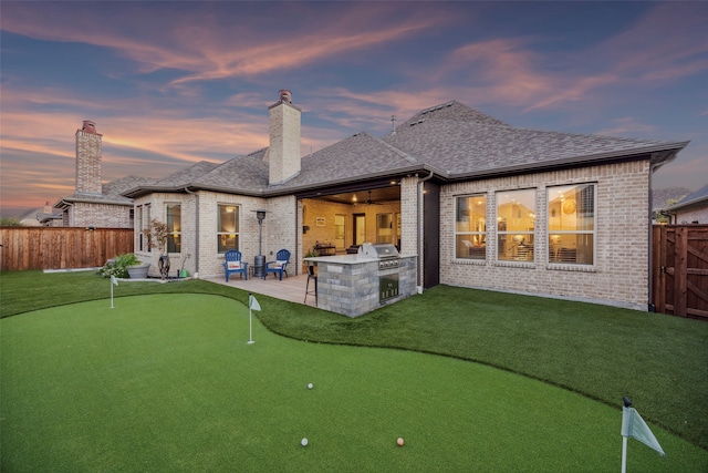 back house at dusk with a patio area and an outdoor kitchen