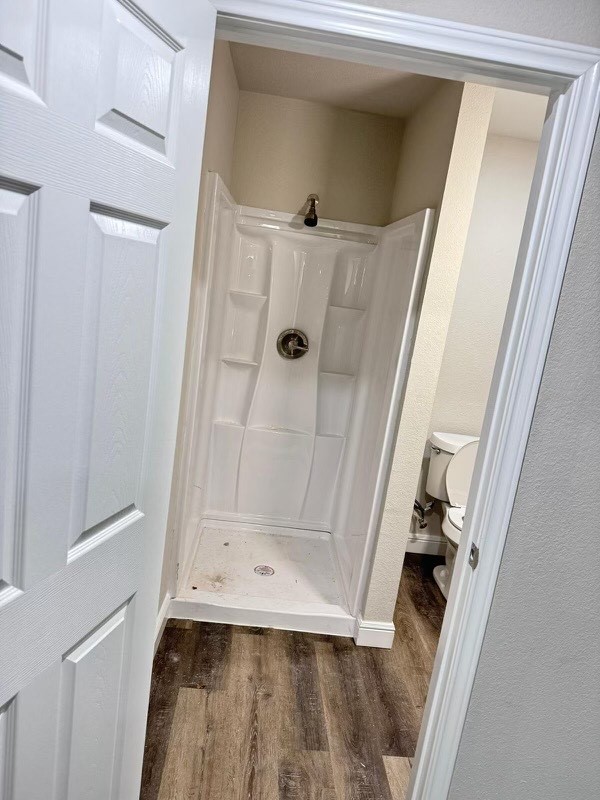 bathroom featuring a shower, wood-type flooring, and toilet