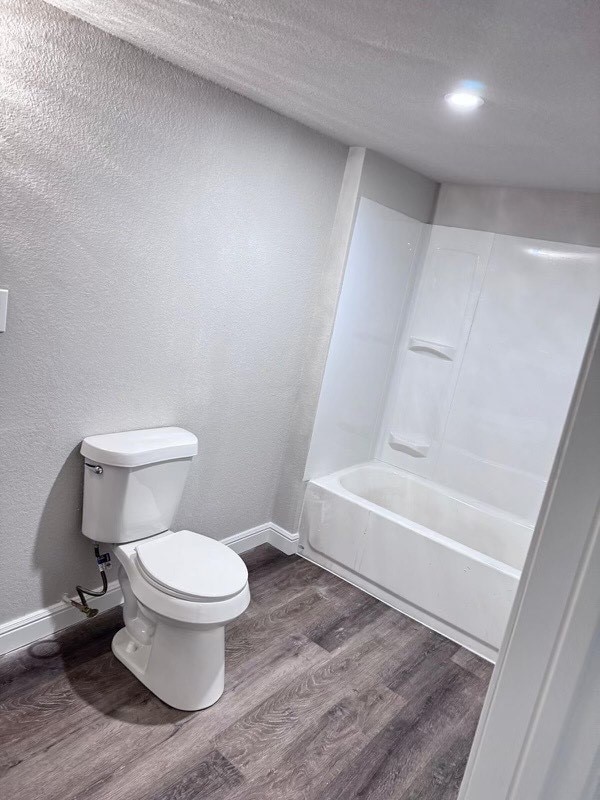 bathroom with toilet, shower / bath combination, wood-type flooring, and a textured ceiling