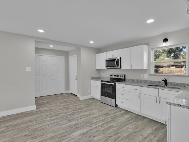 kitchen featuring appliances with stainless steel finishes, sink, light wood-type flooring, white cabinets, and light stone counters