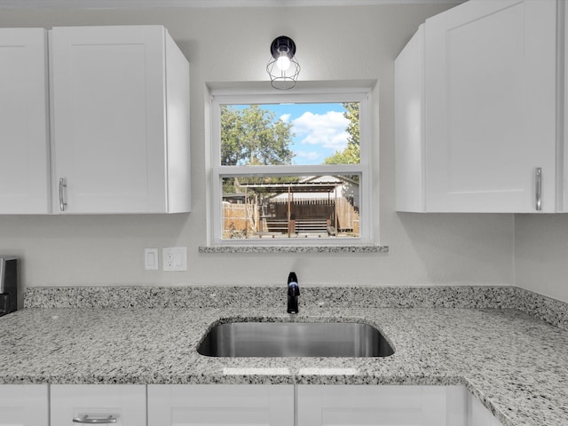 kitchen with light stone countertops, sink, and white cabinets