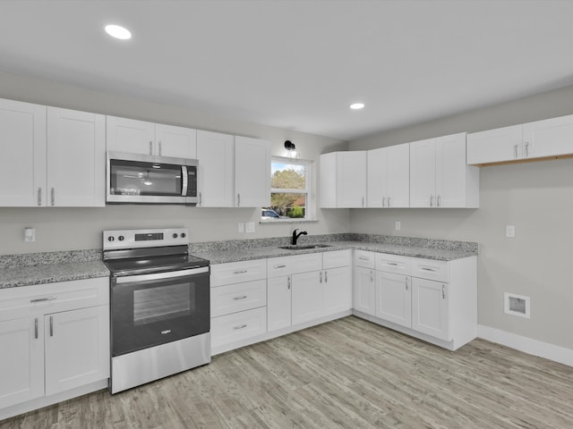 kitchen with white cabinets, appliances with stainless steel finishes, light stone countertops, light wood-type flooring, and sink