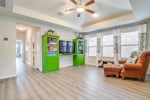 sitting room with ceiling fan, light wood-type flooring, and a tray ceiling