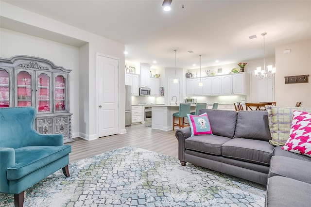 living room featuring sink, light hardwood / wood-style floors, and a notable chandelier