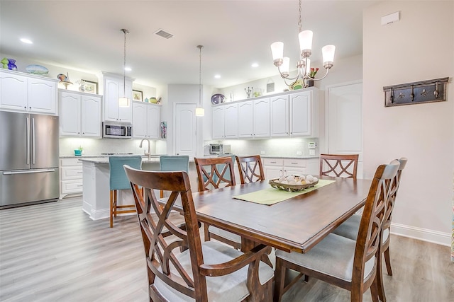 dining area with an inviting chandelier, light hardwood / wood-style flooring, and sink