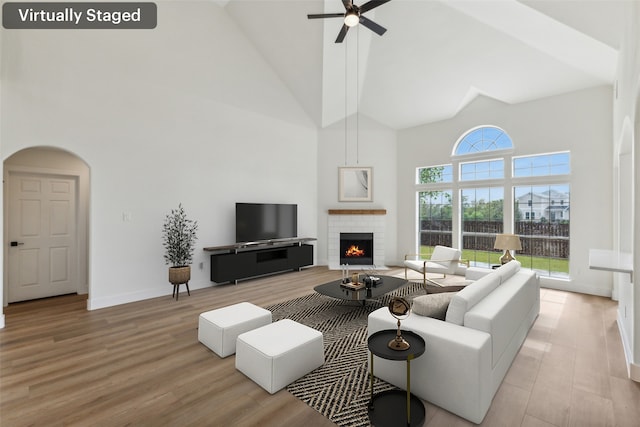 living room with high vaulted ceiling, ceiling fan, a brick fireplace, and light hardwood / wood-style flooring