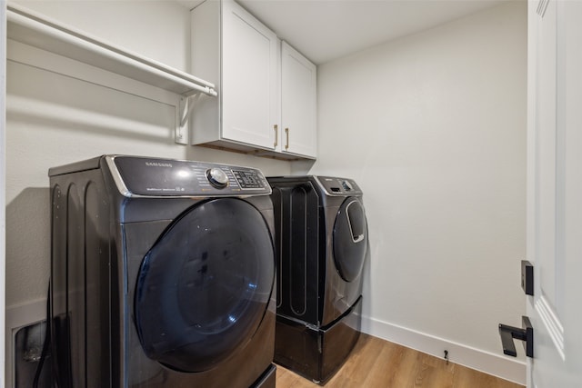 clothes washing area with cabinets, washing machine and clothes dryer, and light hardwood / wood-style flooring