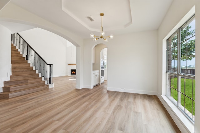 interior space featuring light hardwood / wood-style flooring, a notable chandelier, a raised ceiling, and plenty of natural light