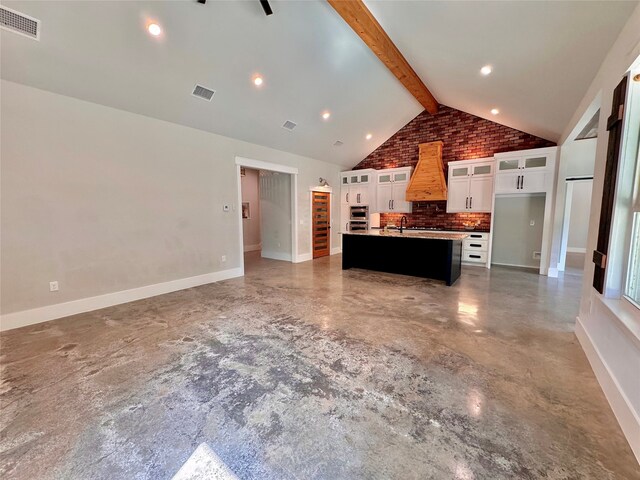 kitchen featuring decorative backsplash, a center island with sink, white cabinets, lofted ceiling with beams, and premium range hood