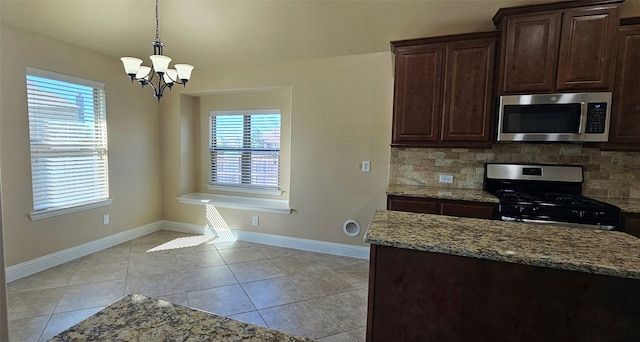 kitchen with light stone countertops, appliances with stainless steel finishes, tasteful backsplash, dark brown cabinetry, and a notable chandelier