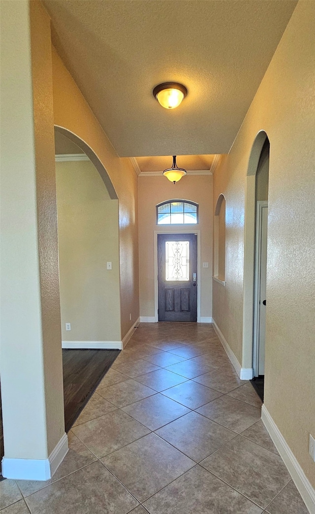 foyer entrance featuring a textured ceiling, light tile patterned floors, and crown molding